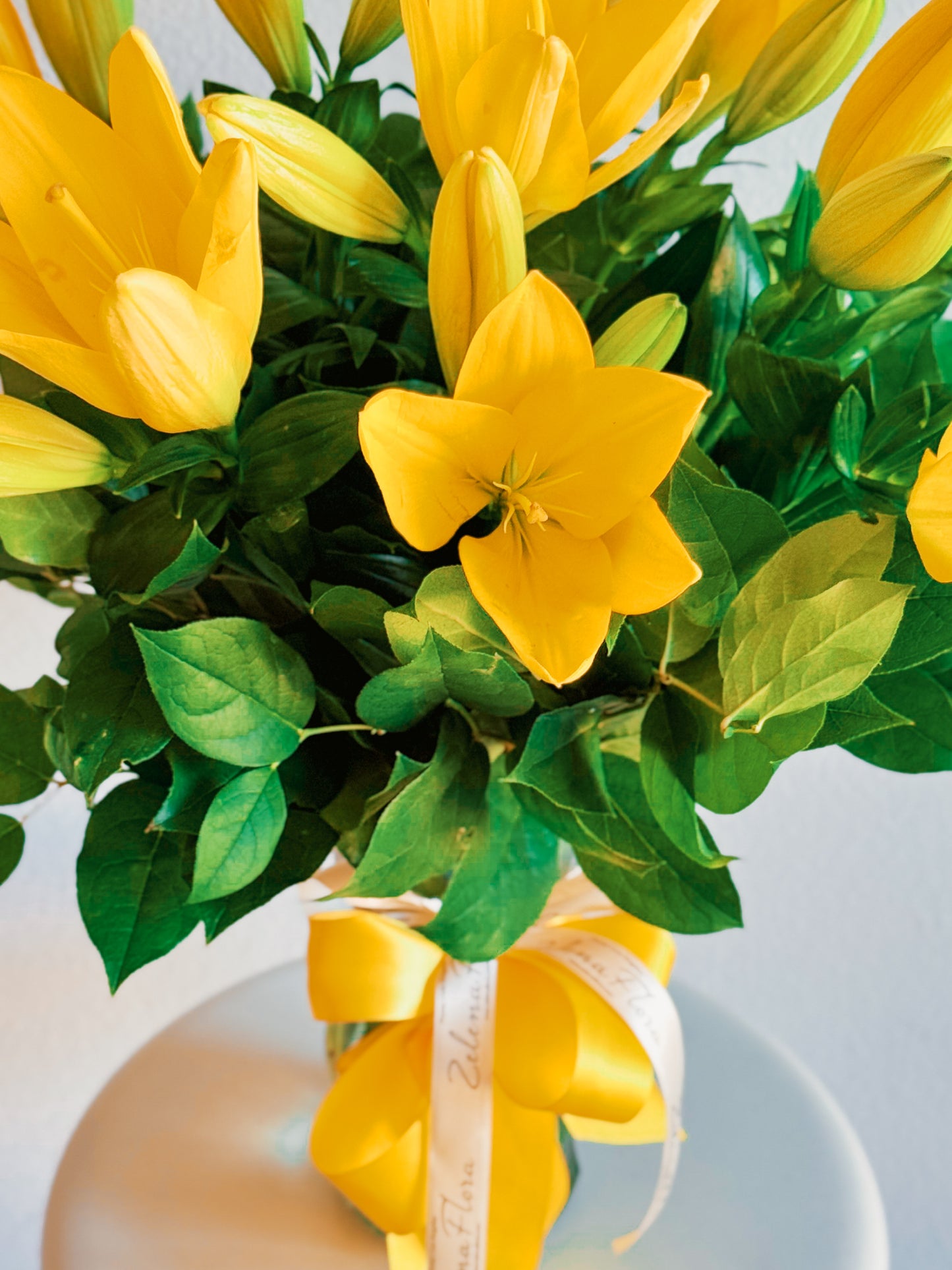 Bouquet of yellow flowers with green leaves in a vase on a light background