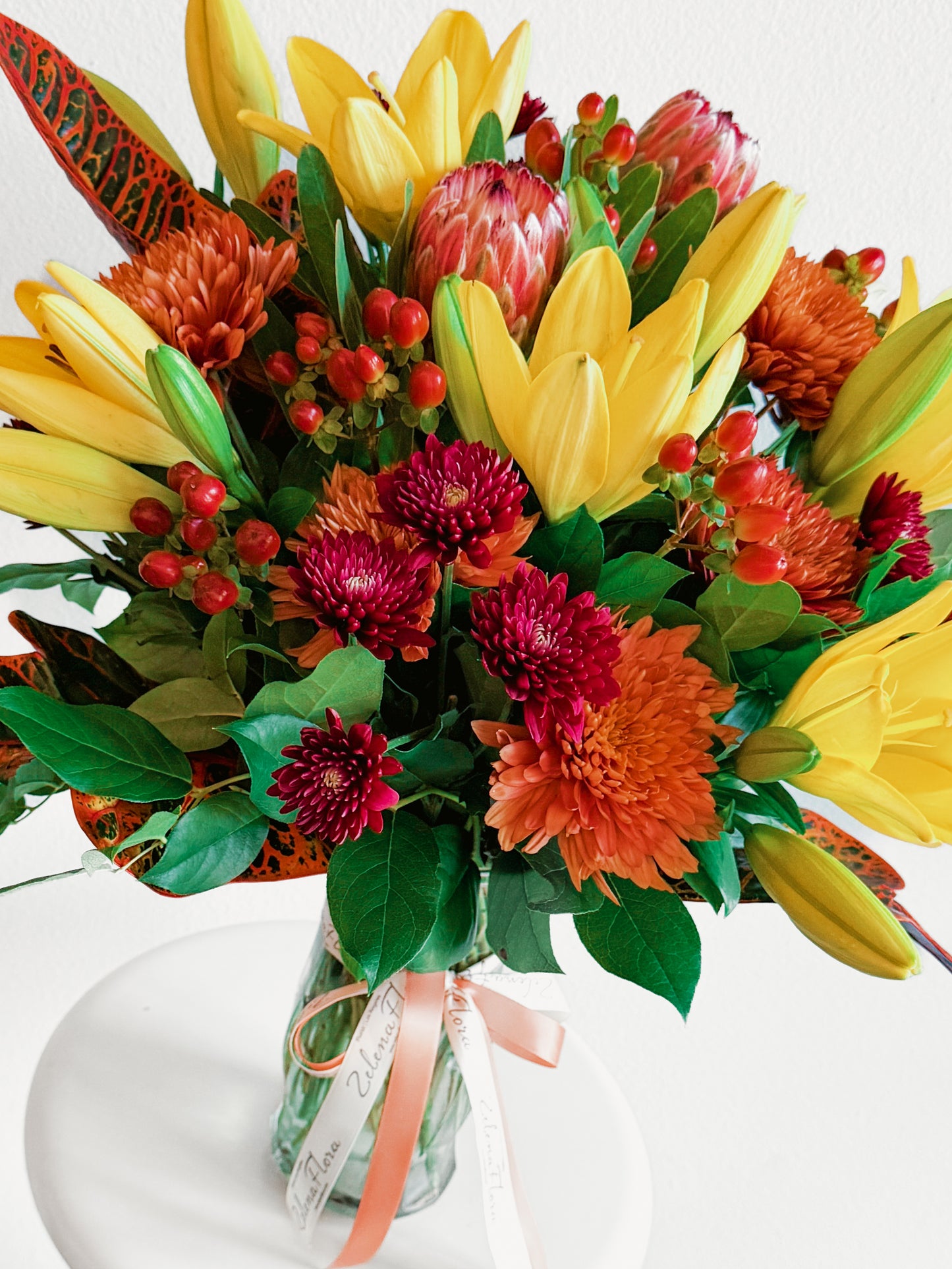 Colorful bouquet of flowers with yellow tulips, red and orange flowers, and green leaves on a white background.