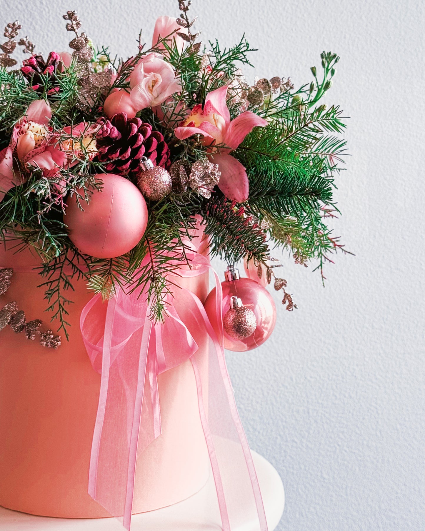 Decorative arrangement with pink ornaments, greenery, and a pink ribbon on a light background