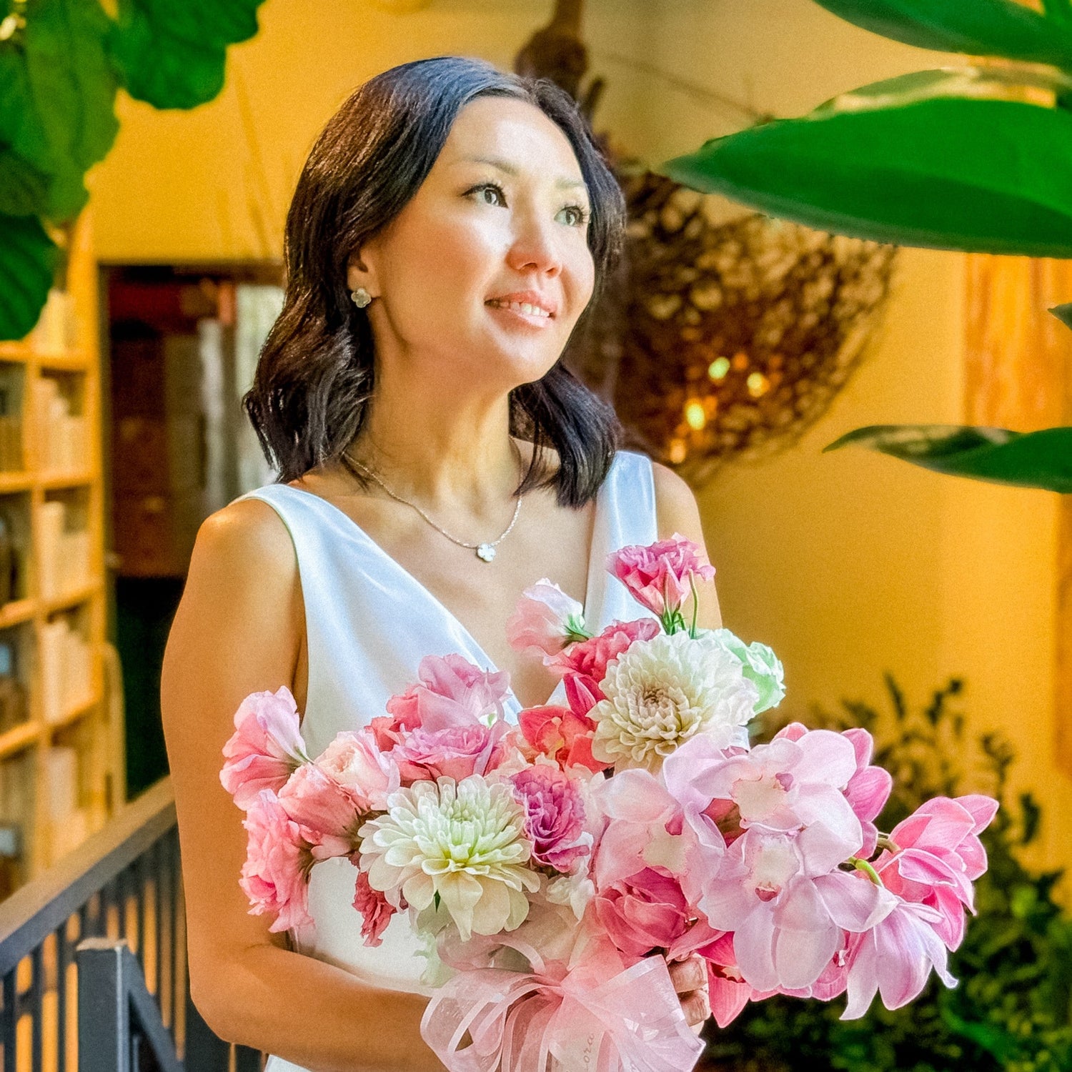Woman in a white dress holding a bouquet of pink and white flowers outdoors.