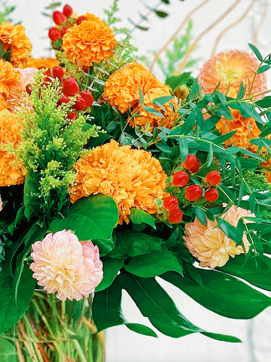 Bouquet of orange marigolds, greenery, and red berries in a clear vase.