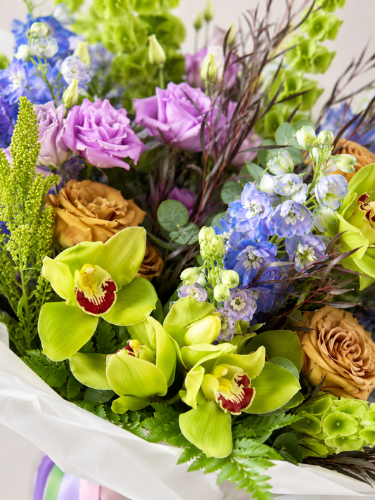 Close-up of Spring Freshness bouquet with green orchids, blue delphinium, lilac lisianthus, roses, Bells of Ireland, stock flowers, and fresh greenery | Zelena Flora | Los Angeles