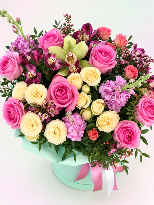 Elevated view of Flower Fantasy pink roses, yellow spray roses, green orchid and lilac stock on a light abstract background