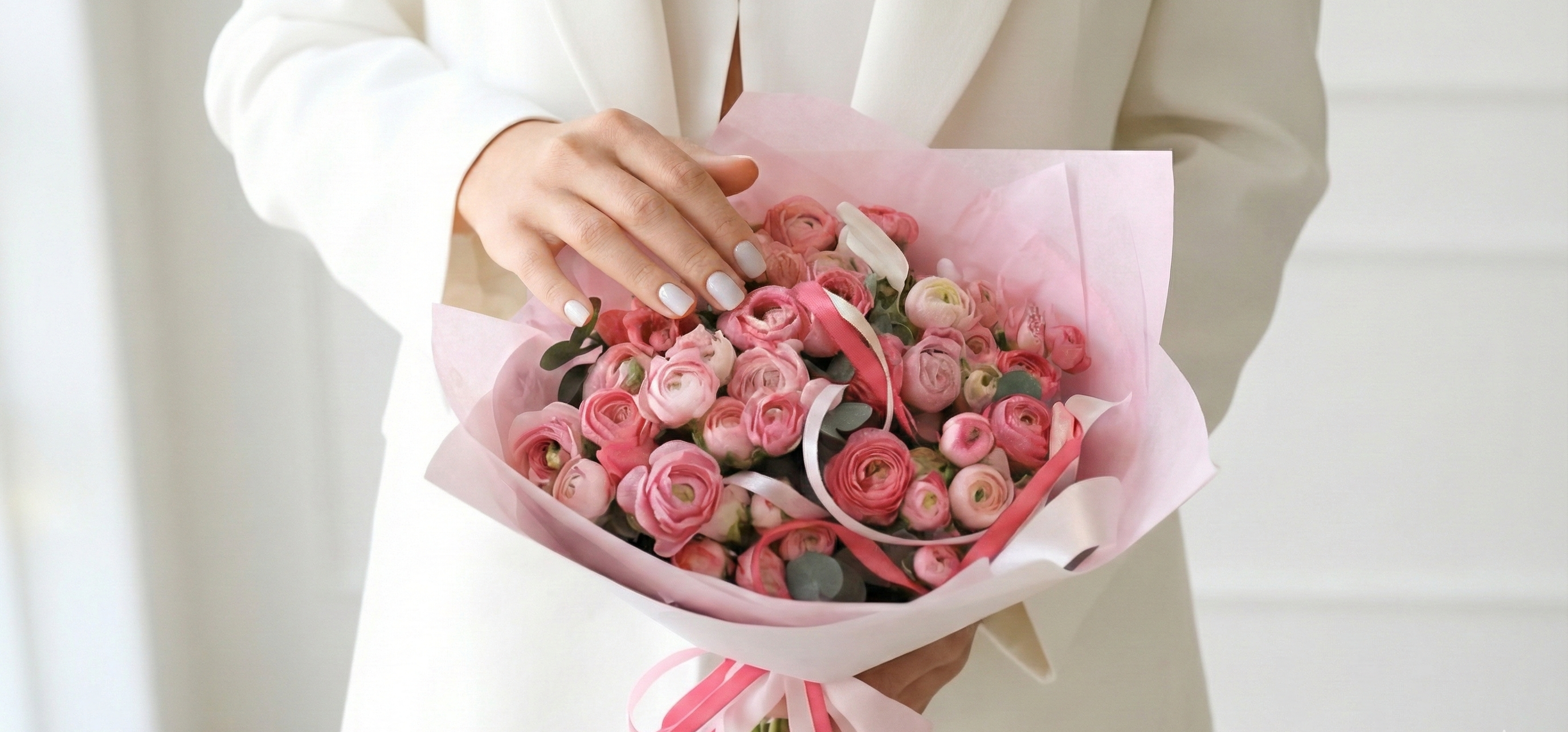 Person holding a bouquet of pink flowers wrapped in pink paper against a neutral background