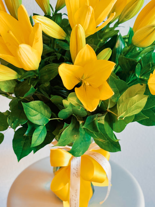 Bouquet of yellow flowers with green leaves in a vase on a light background
