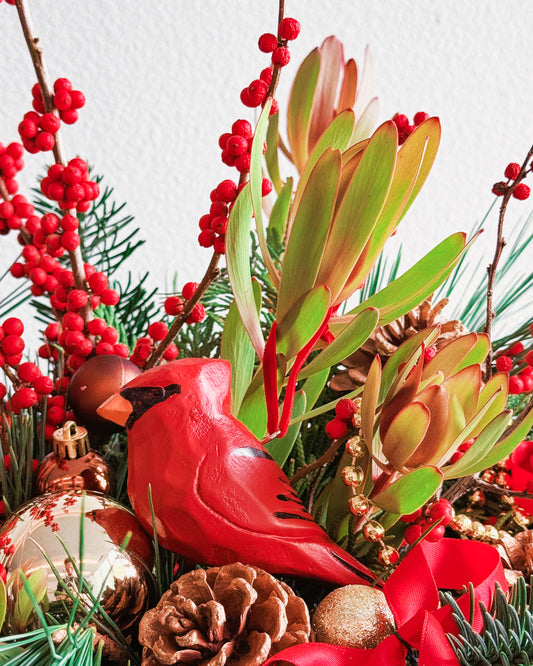 Decorative arrangement with red cardinal figurine, greenery, and red berries on a white background