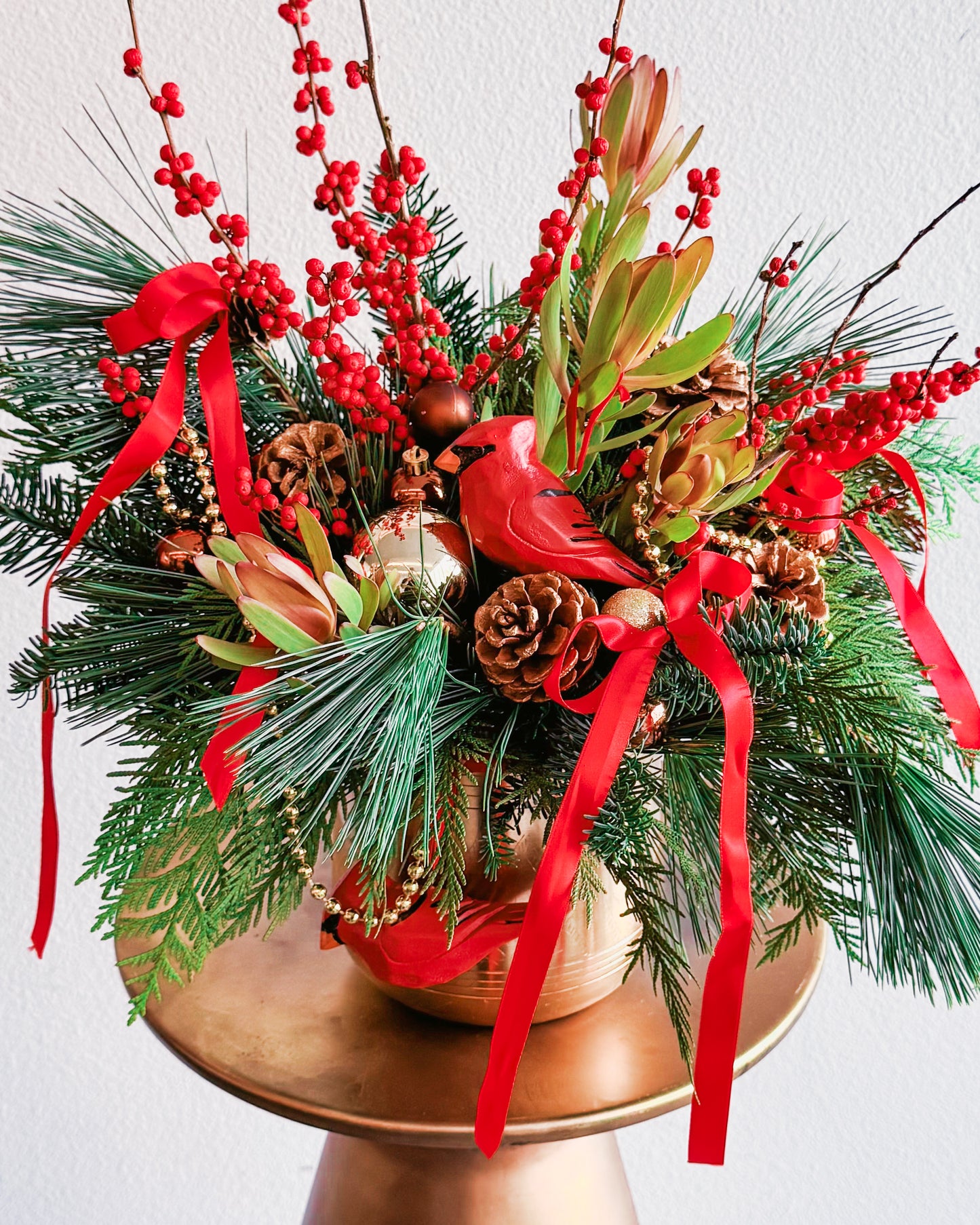 Christmas-themed floral arrangement with red ribbons, pinecones, and berries on a white background