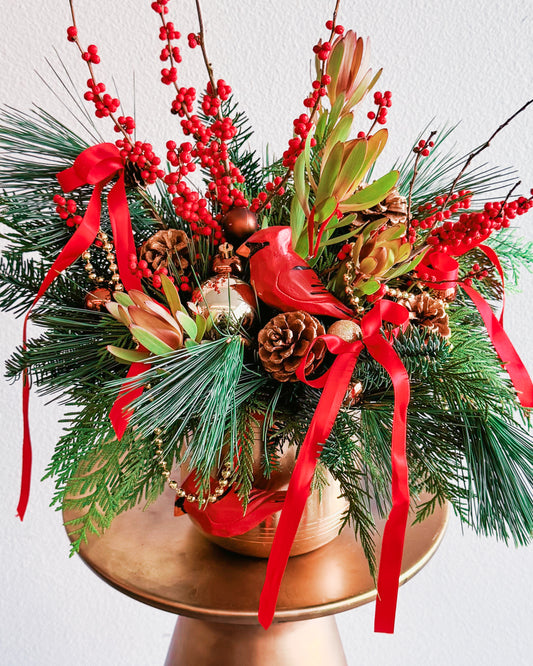 Christmas-themed floral arrangement with red ribbons, pinecones, and berries on a white background