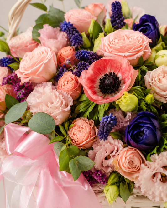 Close-up of Pleasure Hampy basket with pink roses, ranunculus, coral anemone, blue muscari, purple accents, eucalyptus, and satin ribbon | Zelena Flora | Los Angeles