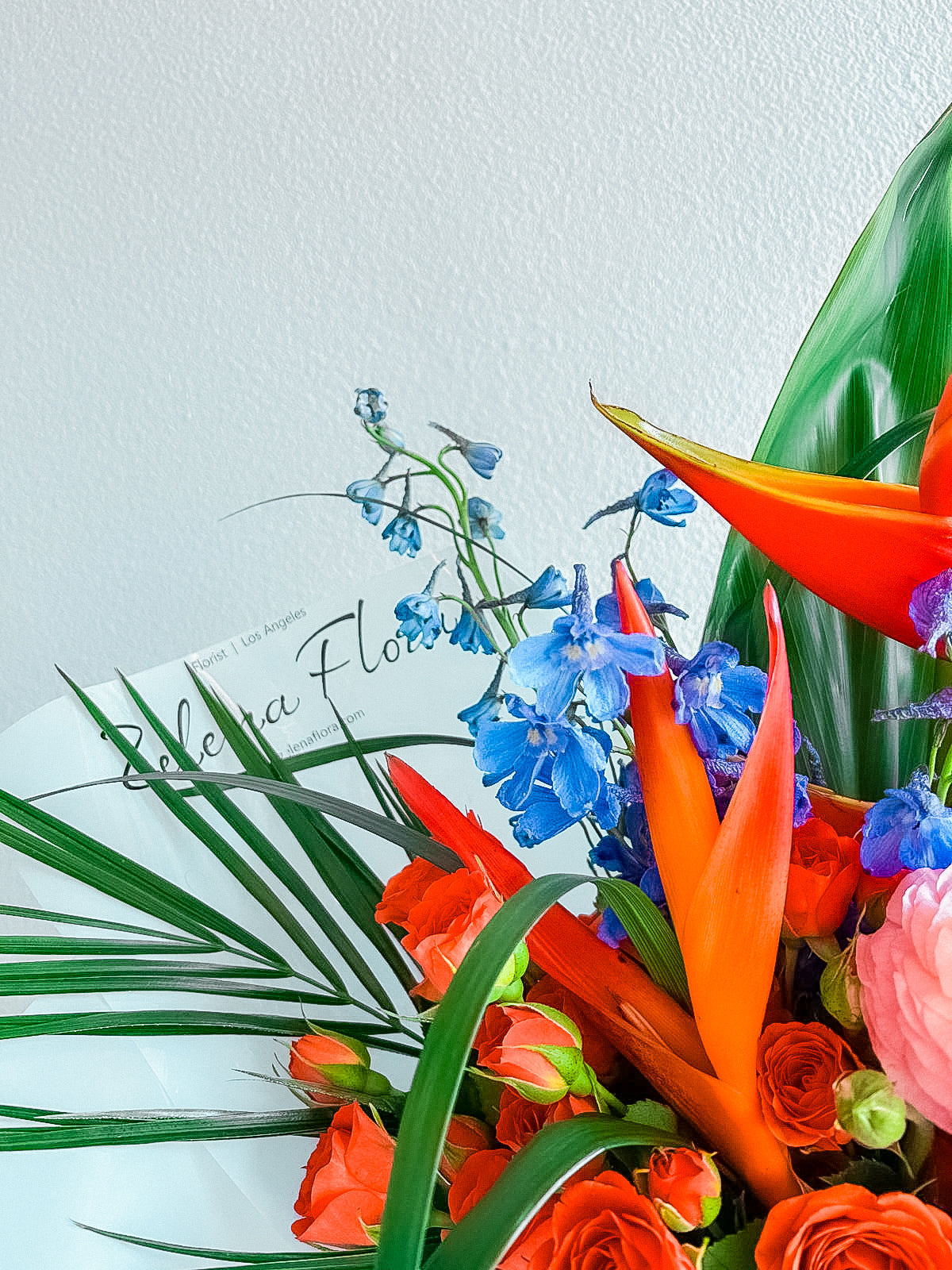Spice Bloom by Zelenaflora, a tropical spring bouquet with orange spray roses, pink ranunculus, blue delphinium, purple statice, and sculptural greenery in Los Angeles
