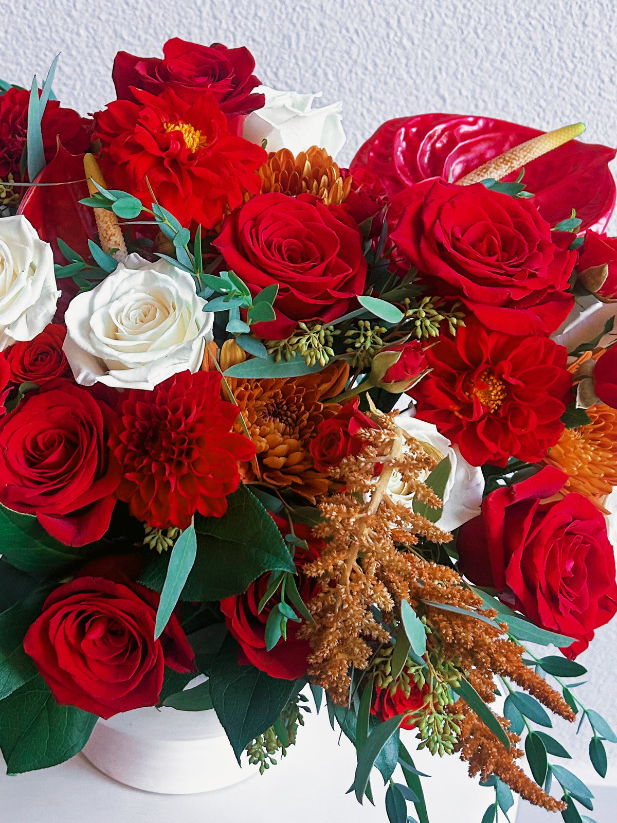 Crimson Charm flower detail showing red roses, white roses, red dahlias, a glossy red anthurium and copper-orange chrysanthemums.