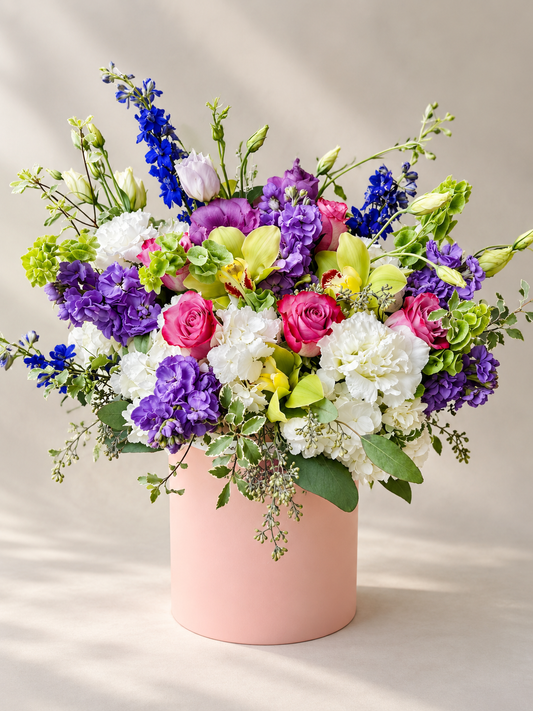 English Garden flower arrangement in a blush pink round box, full studio view with roses, hydrangeas, orchids and blue delphinium