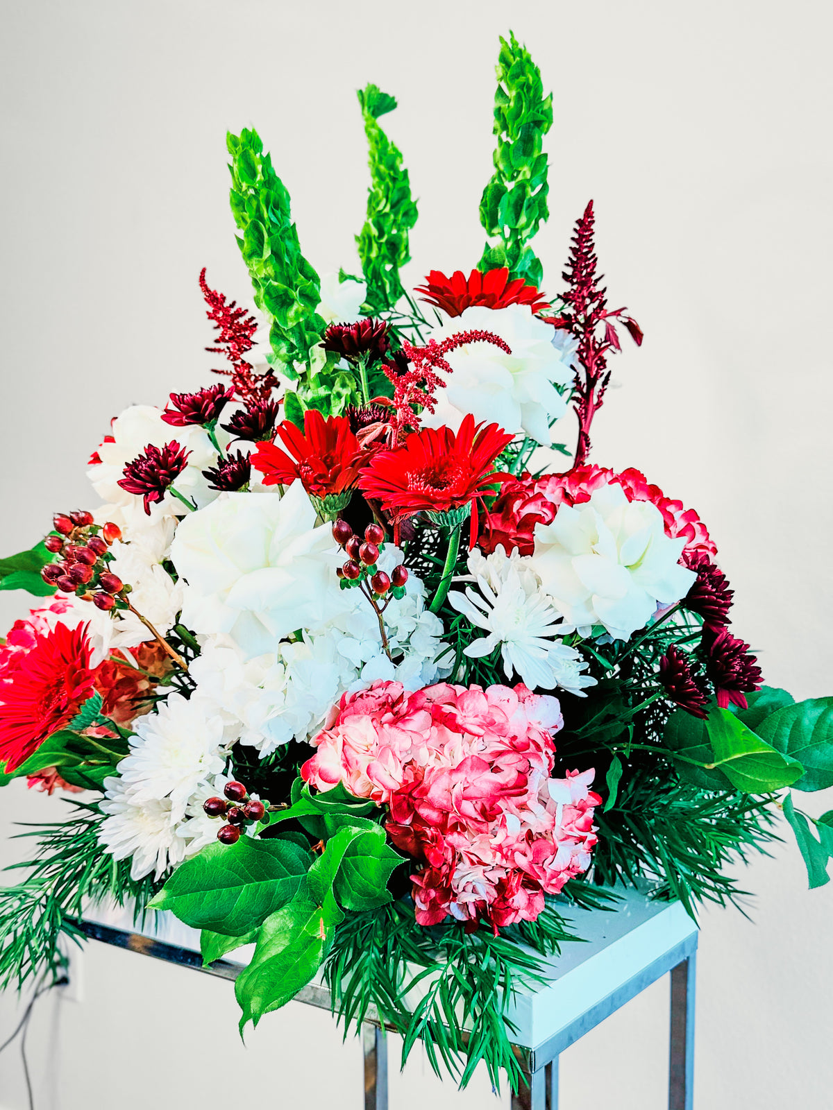 Closer view of Floral Fanfare with red gerberas, ivory roses, pink and white hydrangeas, burgundy chrysanthemums and leafy greenery.