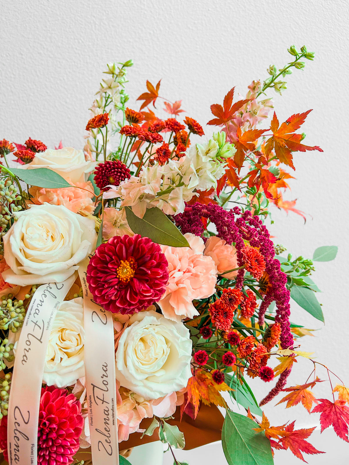 Floral Fresco detail showing a burgundy dahlia, peach carnations, ivory roses, eucalyptus and branded cream ribbon.