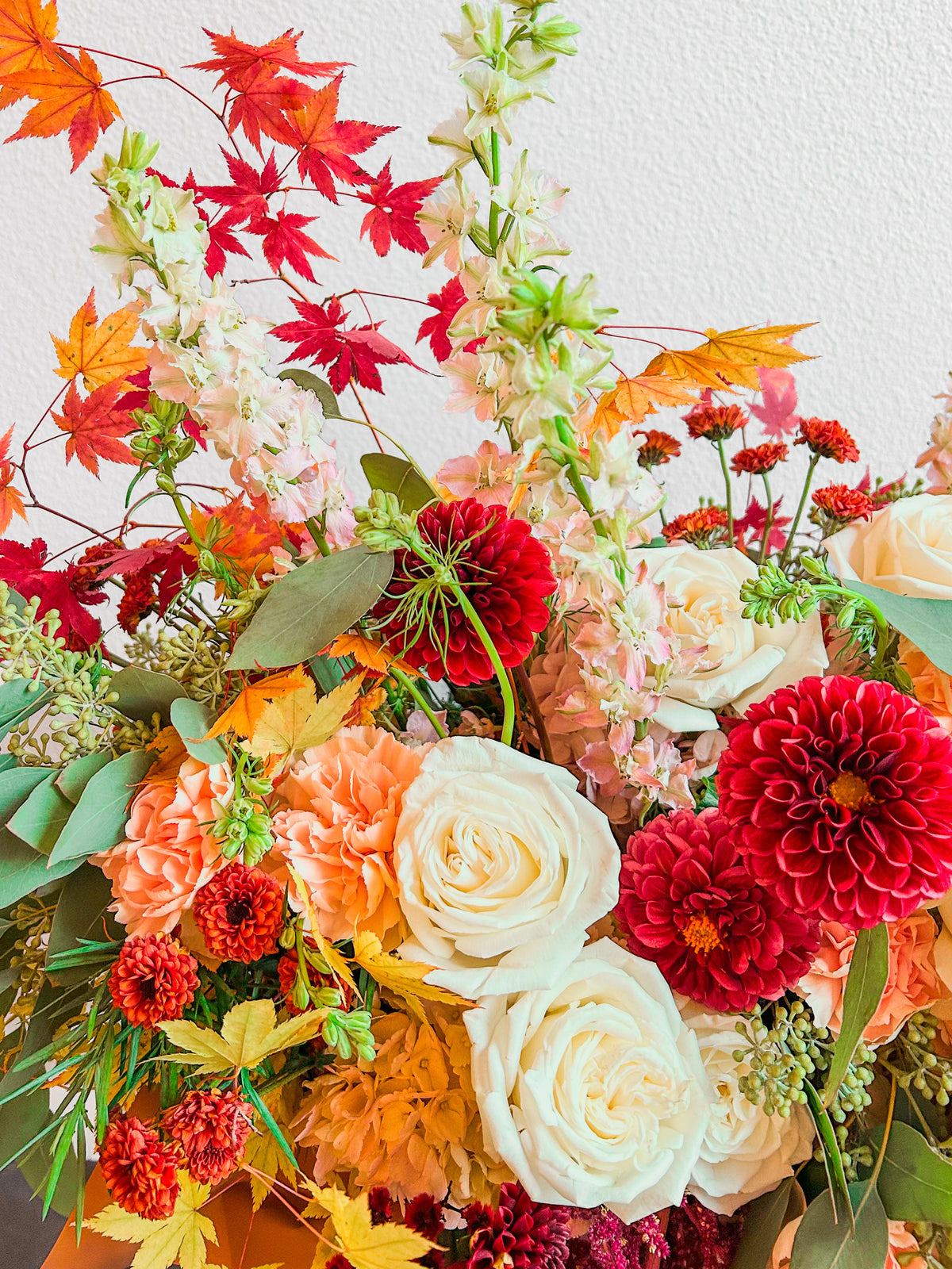 Floral Fresco flower detail with ivory roses, peach carnations, burgundy dahlias and red and golden decorative leaves.