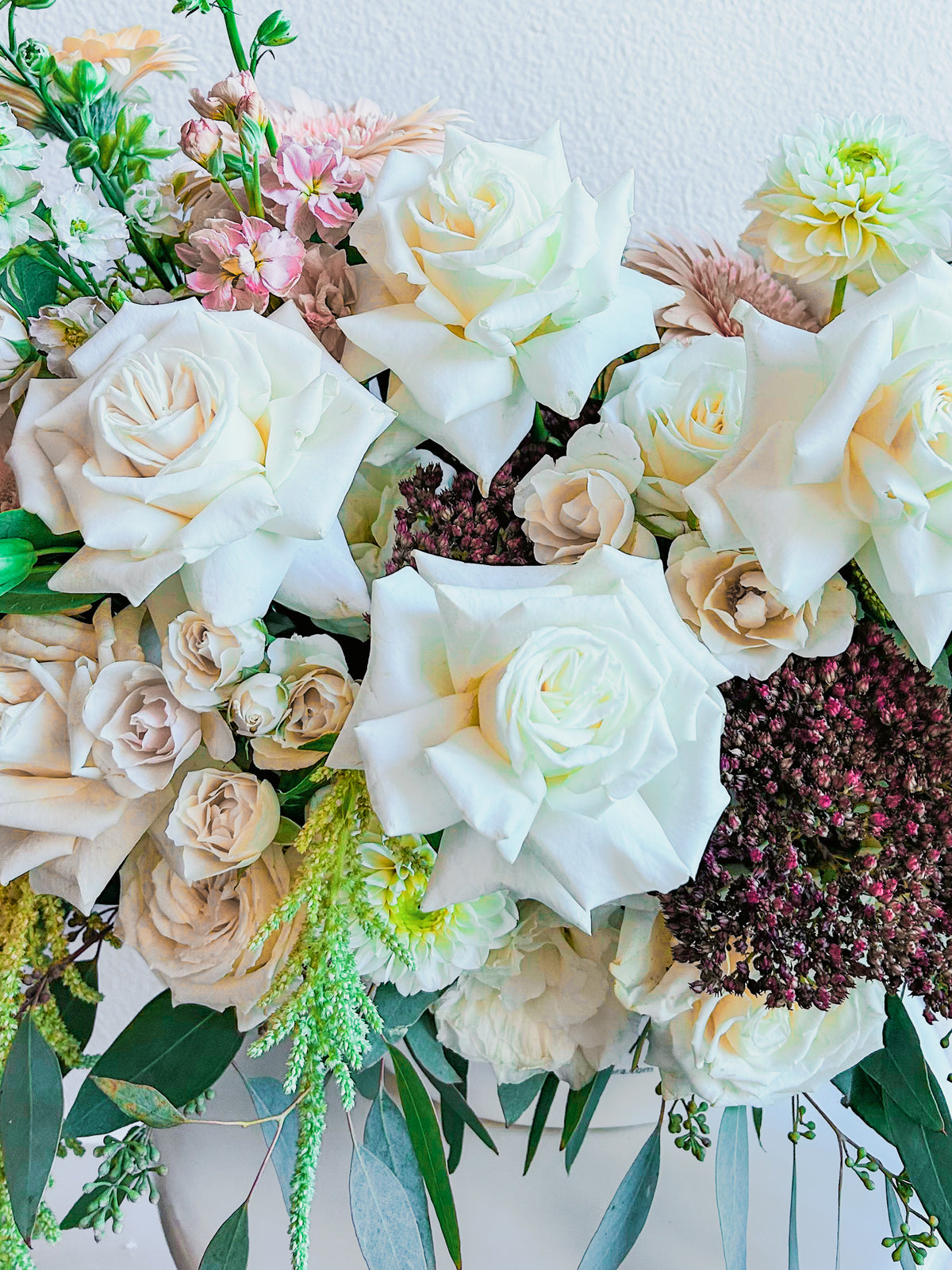 Gentle Gesture flower detail with open ivory roses, cream spray roses, burgundy flower clusters and silver-green eucalyptus.