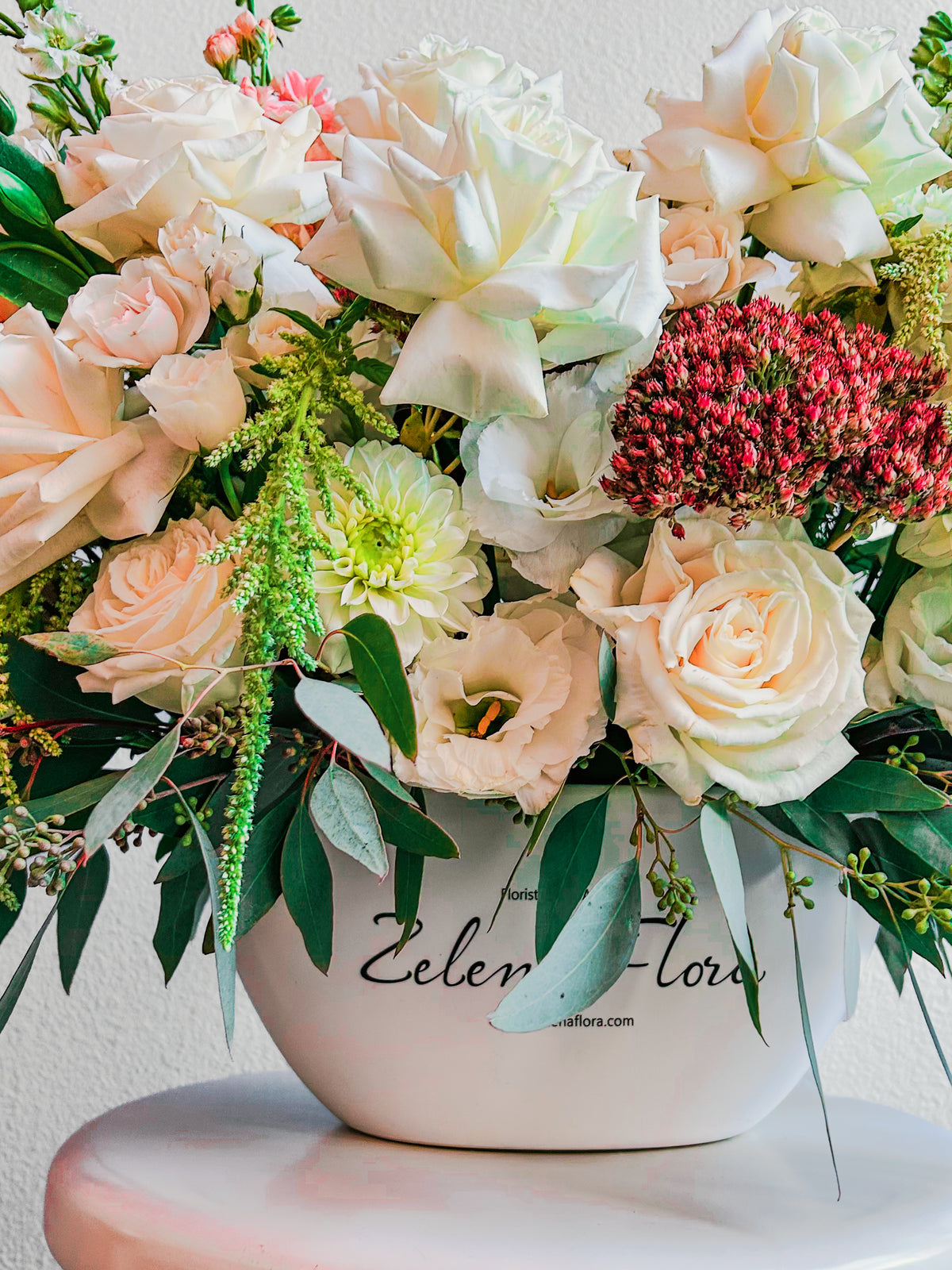 Gentle Gesture vase detail showing pale roses, ruffled cream blooms and trailing green accents above the rounded white branded vase.