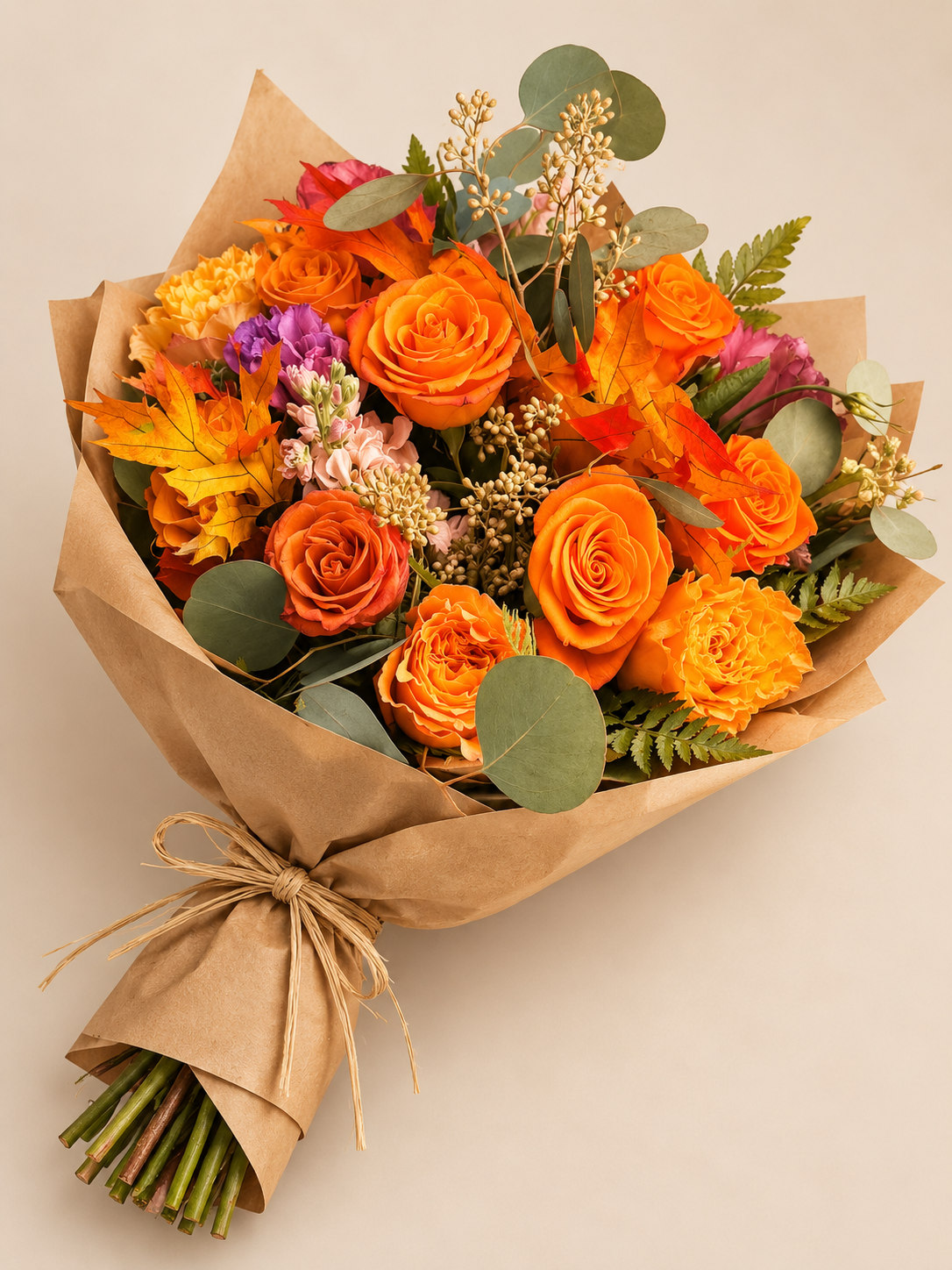 Golden Harvest hand-tied autumn bouquet wrapped in kraft paper with orange roses, chrysanthemums, peach stock, eucalyptus and fall leaves