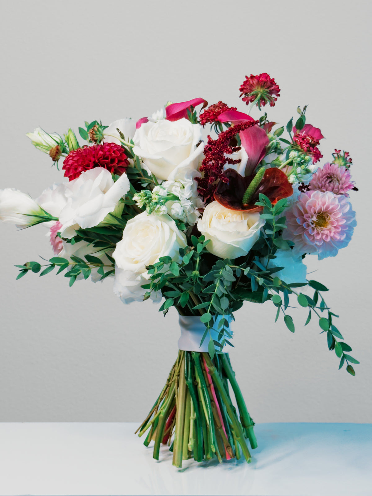 Full Passion Promise bouquet with a pale ribbon, exposed stems and flowing greenery in directional light | Zelena Flora | Los Angeles
