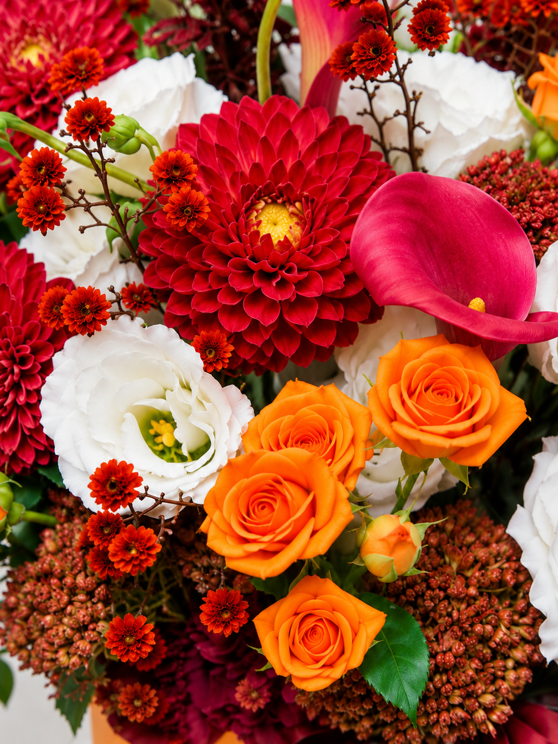 Close-up of a red dahlia, raspberry-pink calla lily, orange spray roses and white lisianthus in Radiant Rhythm.