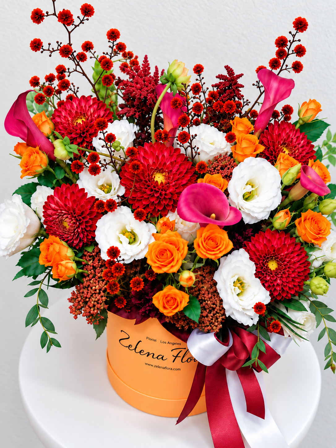 Angled overhead view of Radiant Rhythm with red dahlias, orange spray roses, pink calla lilies and white lisianthus in an orange box.