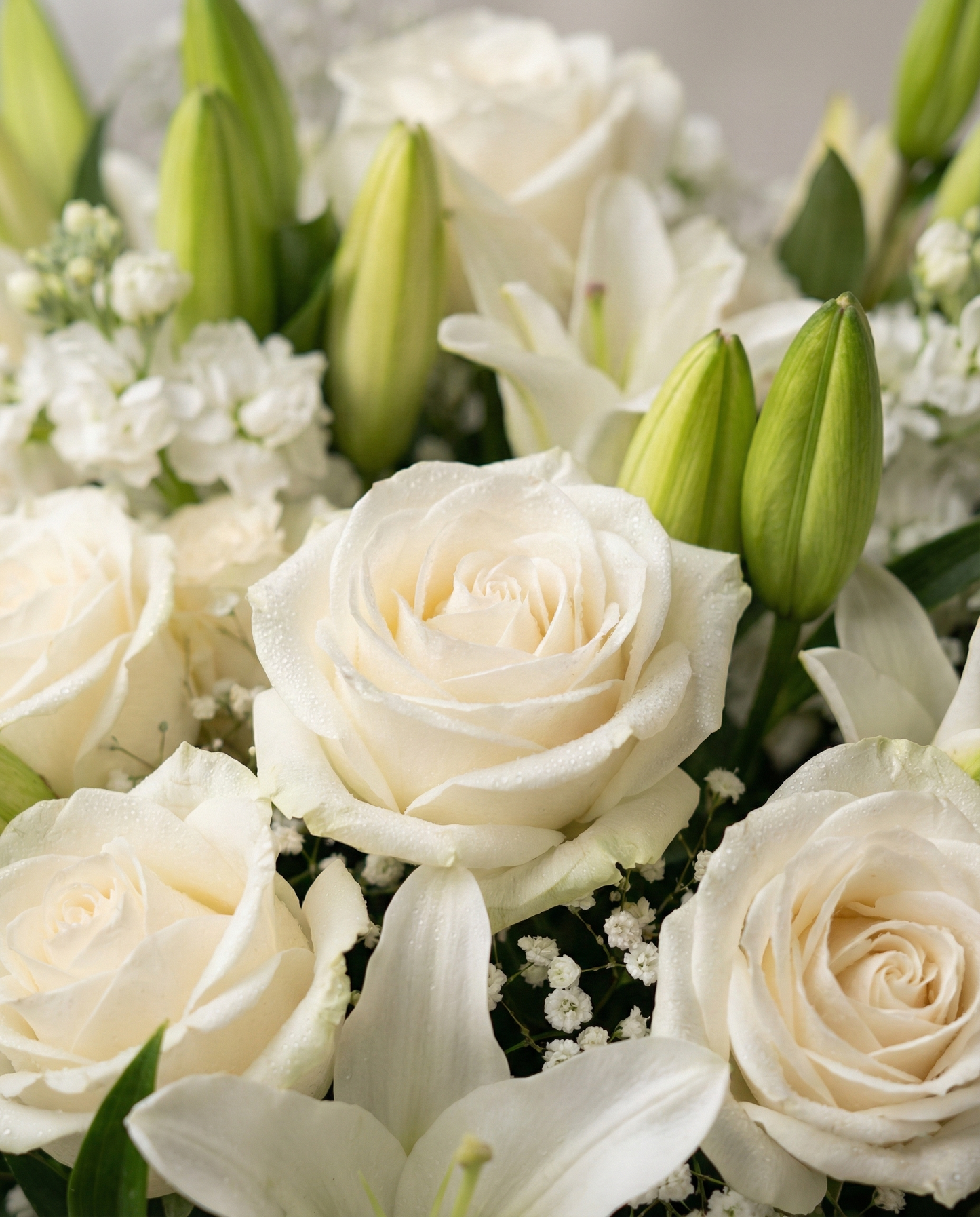 Close-up of a bouquet of white roses and lilies with green buds.